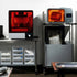 3D printing equipment with a smaller printer on the left and a larger one on the right, surrounded by trays and medical models.